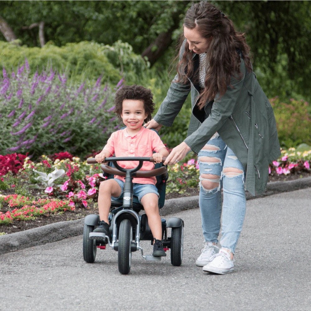 Bentley Trike 6-in-1 V2 Spruce Green child riding with mom guiding on a garden path