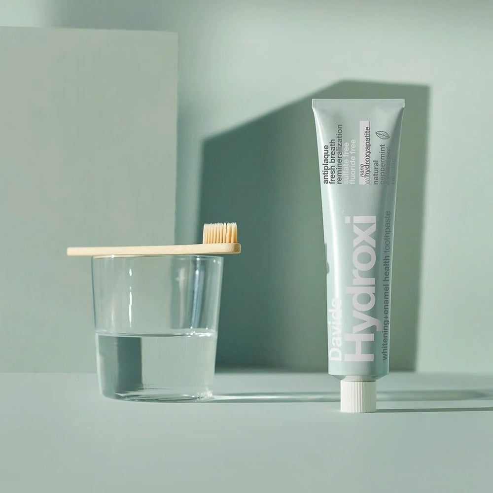 Davids Toothpaste Fluoride Free Peppermint tube stands upright as a bamboo toothbrush rests on a glass of water.