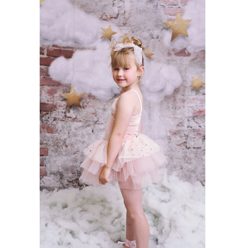 DOLLY BY LE PETIT TOM Stars & Moon tulle hair scrunchie in ballet pink, worn by a girl in a pink tutu against a star backdrop