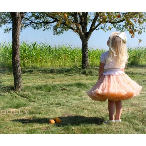 Dolly by Le Petit Tom Dolly Princess & the Frog Pettiskirt Pale Apricot; a girl twirls in a white top outdoors, showing the airy tulle skirt.