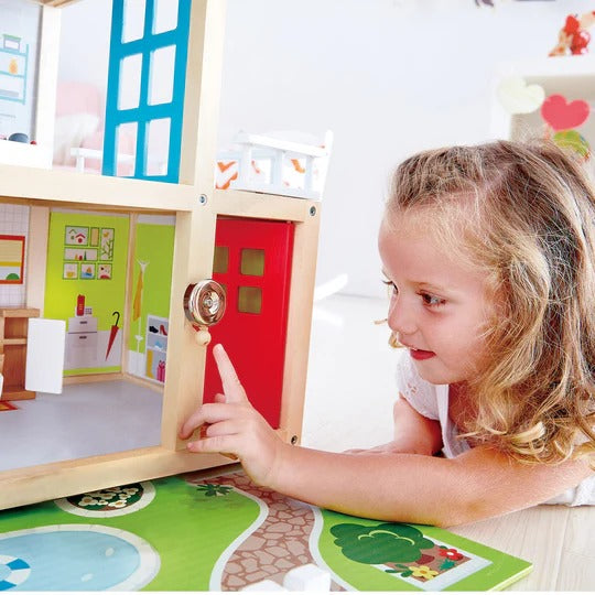 Hape Doll Family Mansion dollhouse with bright rooms; a girl turns the red door knob, sparking imaginative play.