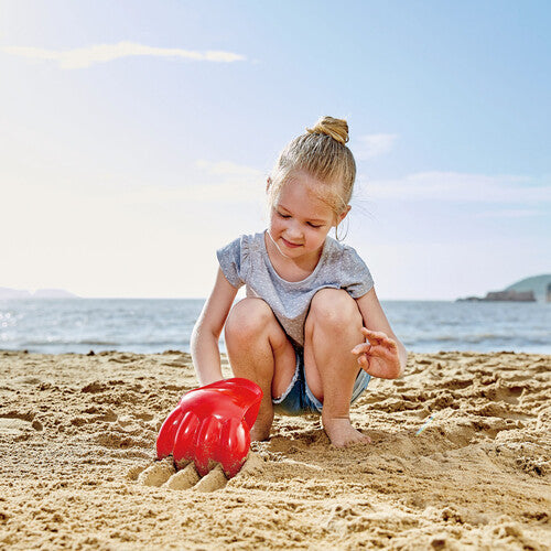 Hape Power Paw Red sand toy; red claw-shaped shovel used by a child playing on the beach.