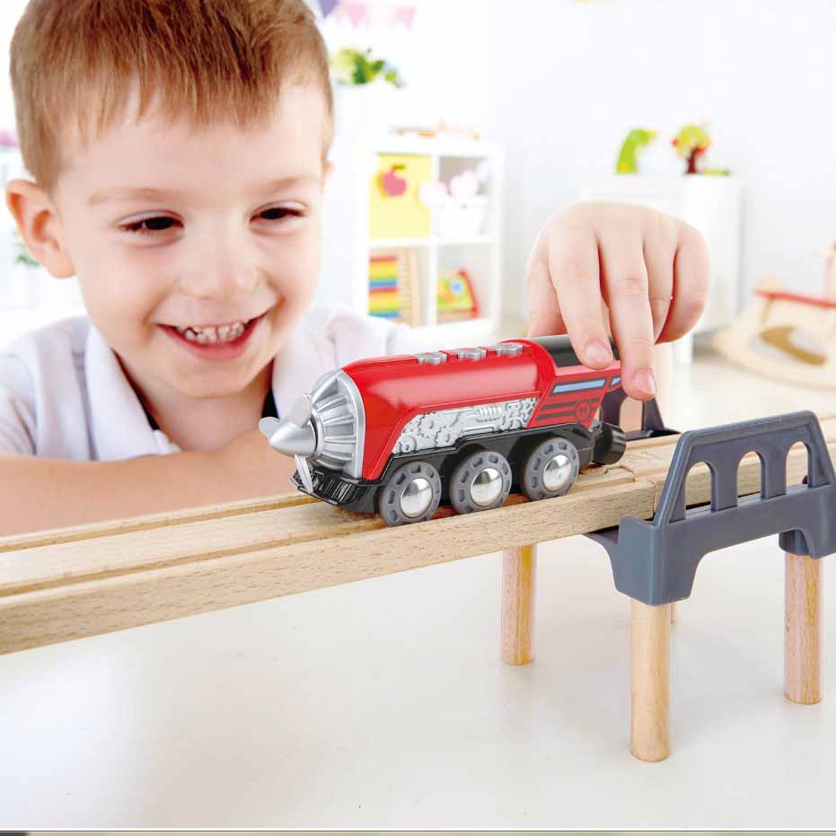Hape Propeller Engine toy train in red with gray wheels, pushed along a wooden track by a smiling child.