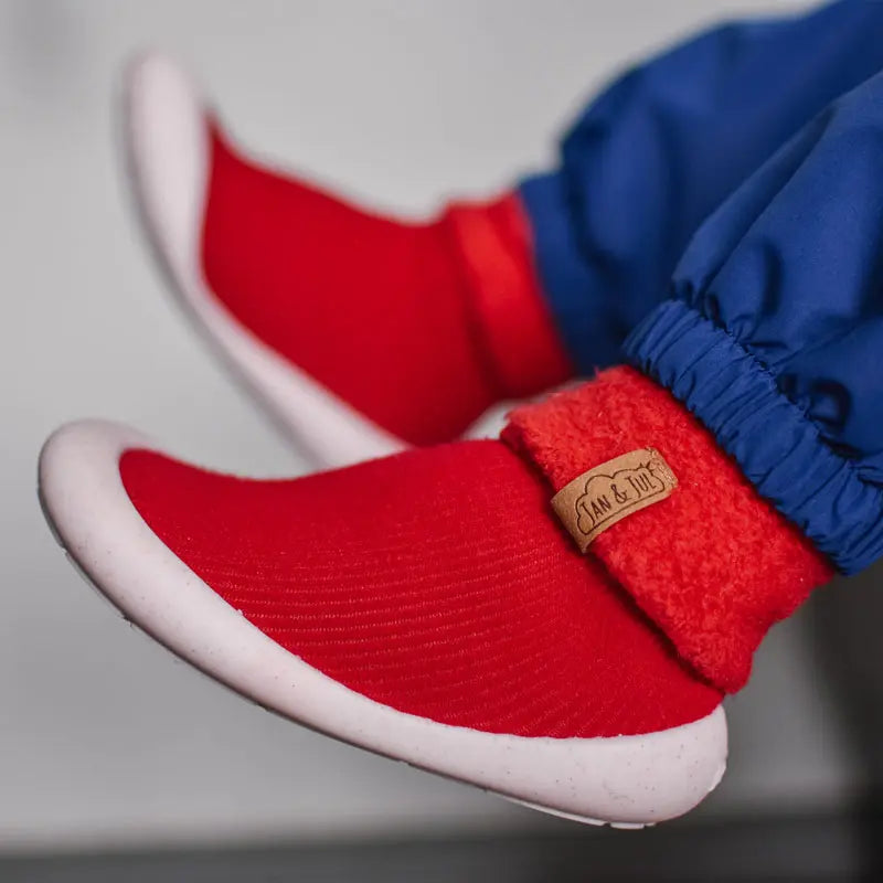 Jan & Jul Cozy Sock Shoes Red baby footwear; red knit upper with white sole, worn with blue pants.