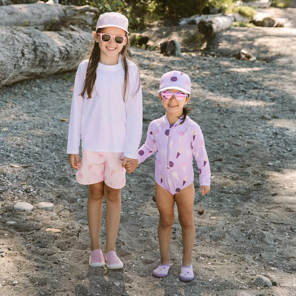 JAN & JUL Girls One Piece UV Swimsuit Lavender Ice Cream; two girls in lavender ice-cream print swimsuits hold hands on a bright beach.