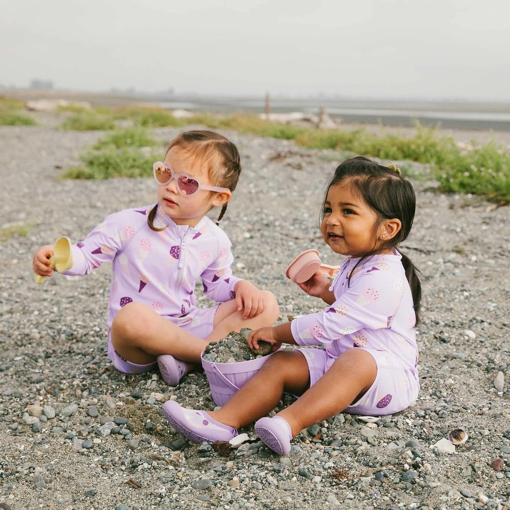 JAN & JUL Kids One Piece UV Sun Suit Lavender Ice Cream; two toddlers play with buckets on a rocky beach.