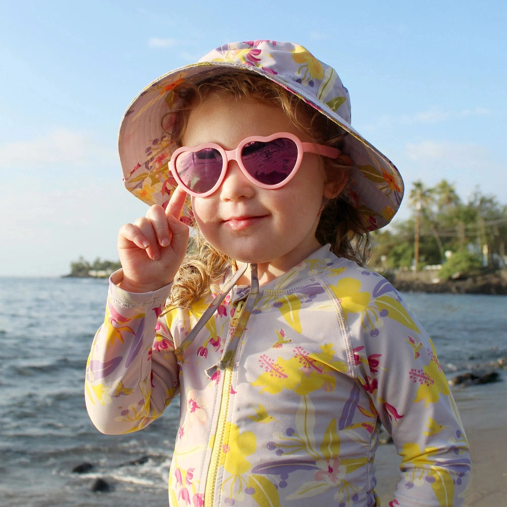 Jan & Jul kids polarized heart sunglasses peachy pink with pink lenses, worn by a child at the beach
