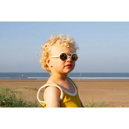 Ki Et La Sunglasses Ourson Cream: baby on beach wearing round cream frames with a yellow outfit