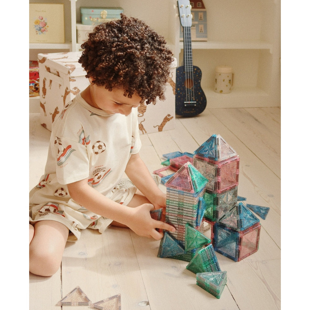 Konges Slojd Basic Two-Piece Cream Outfit with prints; child playing with colorful translucent geometric blocks.