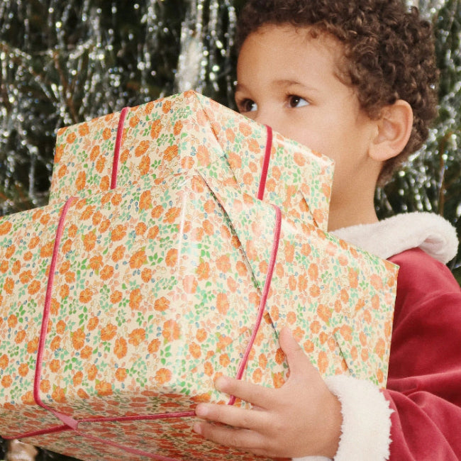 Konges Slojd Christmas Set Red Dahlia for babies/toddlers, a child gently holds a large floral gift box.
