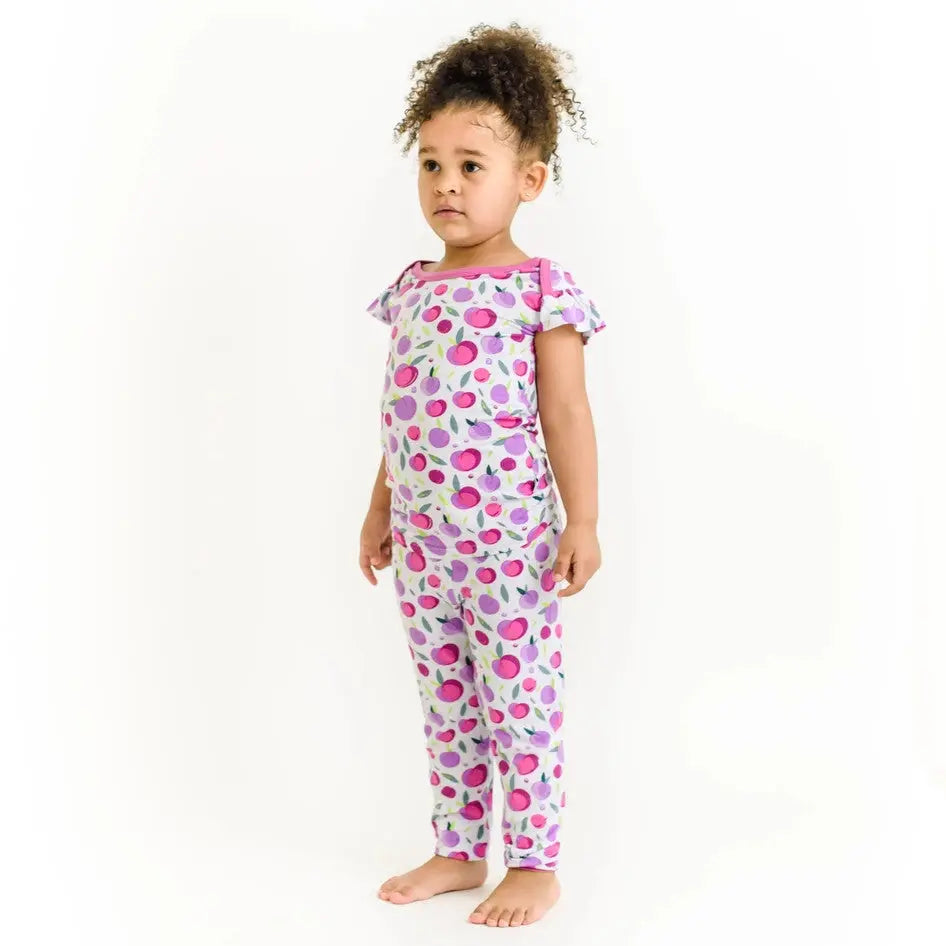 Little Sleepies Bamboo Pajama Set Plum worn by a toddler standing, pink-purple fruit print highlights soft bamboo fabric.