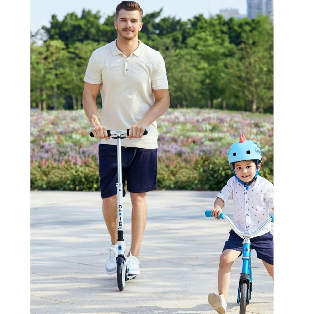 Micro Classic White Scooter; adult rider and a child on a blue balance bike in a park