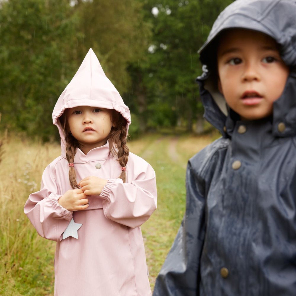 Mini A Ture Matreinar Rain Set Violet Ice: girl in pink hooded raincoat standing in a rainy field.
