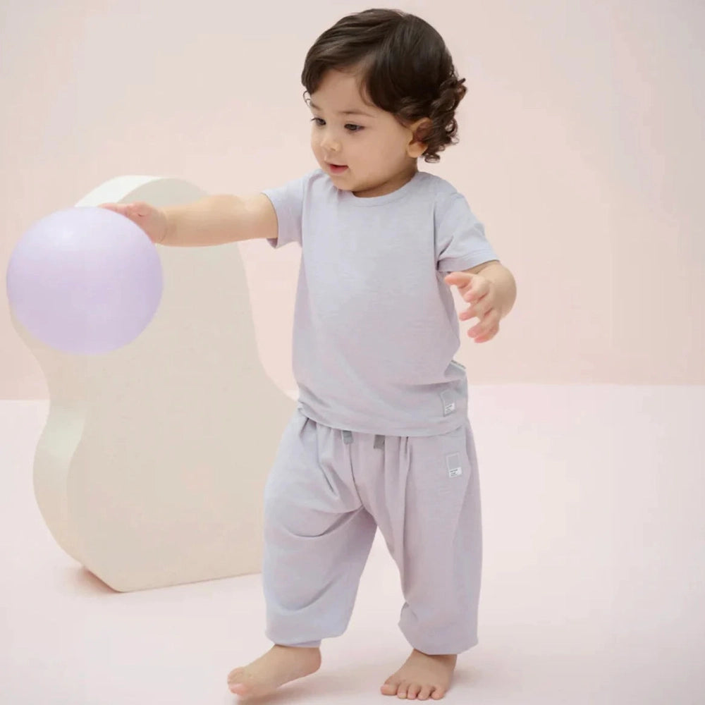 Nest Designs Bamboo Jersey Harem Pants Lavender Blue; toddler walks barefoot, reaching for a pastel ball.