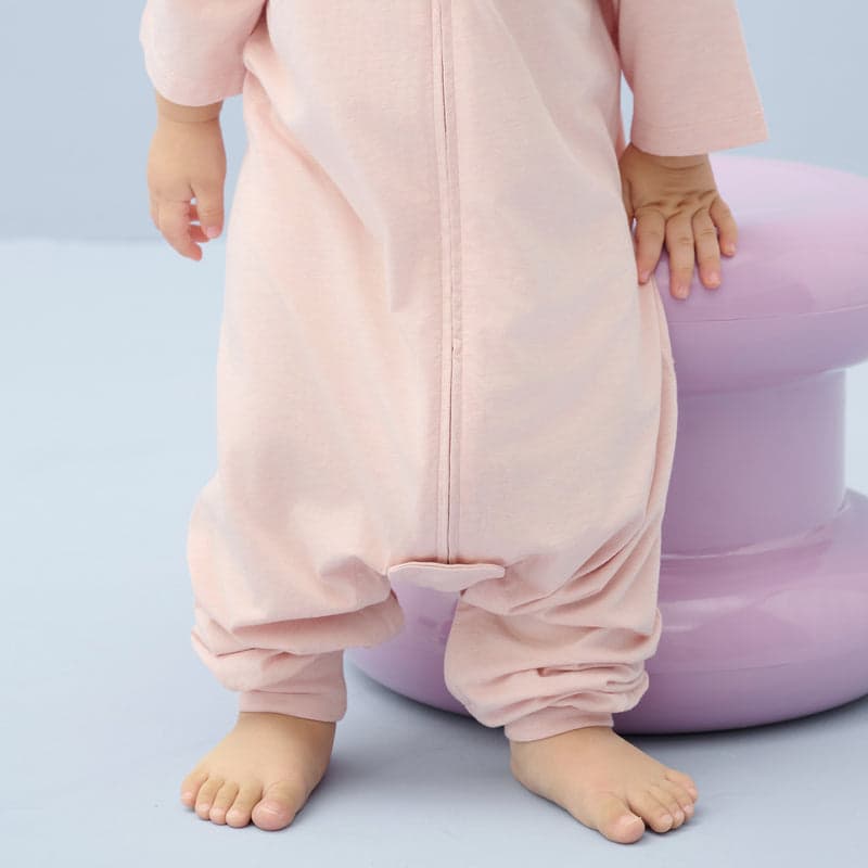Nest Designs Bamboo Jersey Short Sleeve Footed Sleep Bag 0.6 Tog Rose Smoke, baby standing in a soft pink sleep sack with front zipper.