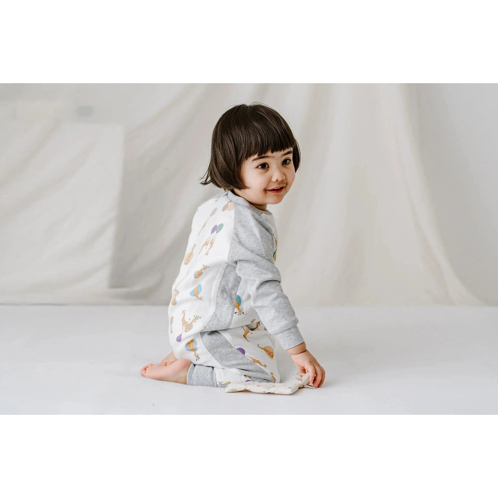 Nest Designs bamboo long-sleeve footed sleep bag 1.0 Tog in giraffe print, toddler sits on the floor wearing it