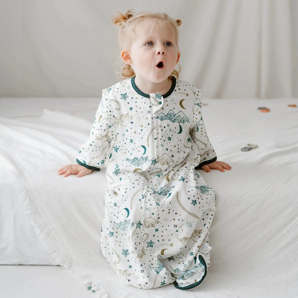 Nest Designs bamboo muslin sleep bag with removable 3/4 sleeves in white star print, toddler sitting on bed.