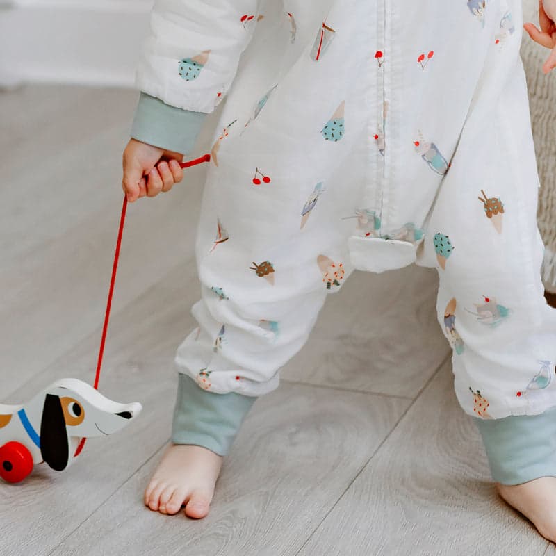 Nest Designs Bamboo Pima Long Sleeve Footed Sleep Bag 0.6 Tog Ice Cream Summer; child pulls red string on a dog toy.