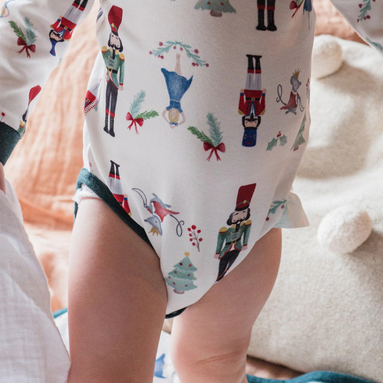 Nest Designs Organic Cotton Long Sleeve Kimono Onesie Nutcracker, white with nutcracker print, worn by a baby.