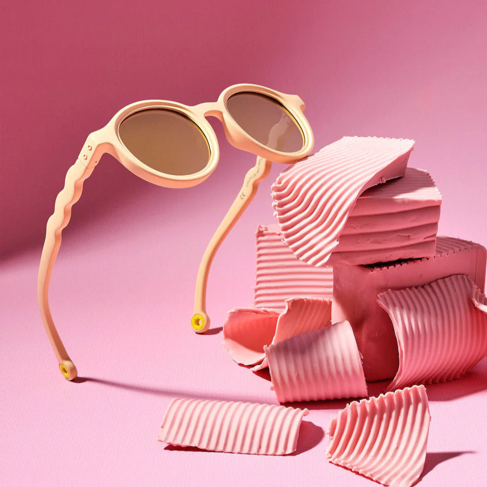 Olivio & Co oval kids sunglasses Desert Sand with wavy arms on pink backdrop