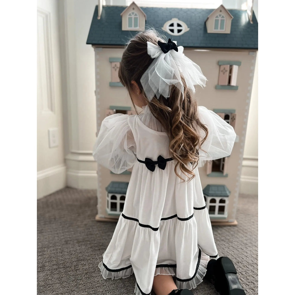 Petit Maison Kids Aurora Ivory Velour Dress worn by a girl twirling, showcasing sheer puff sleeves and black bow trim.