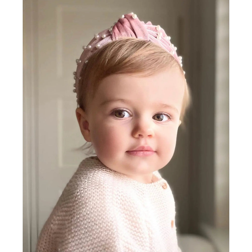 Petite Maison Kids Velvet Pearl Headband, pink velvet with pearls, adorably worn on a baby's head.