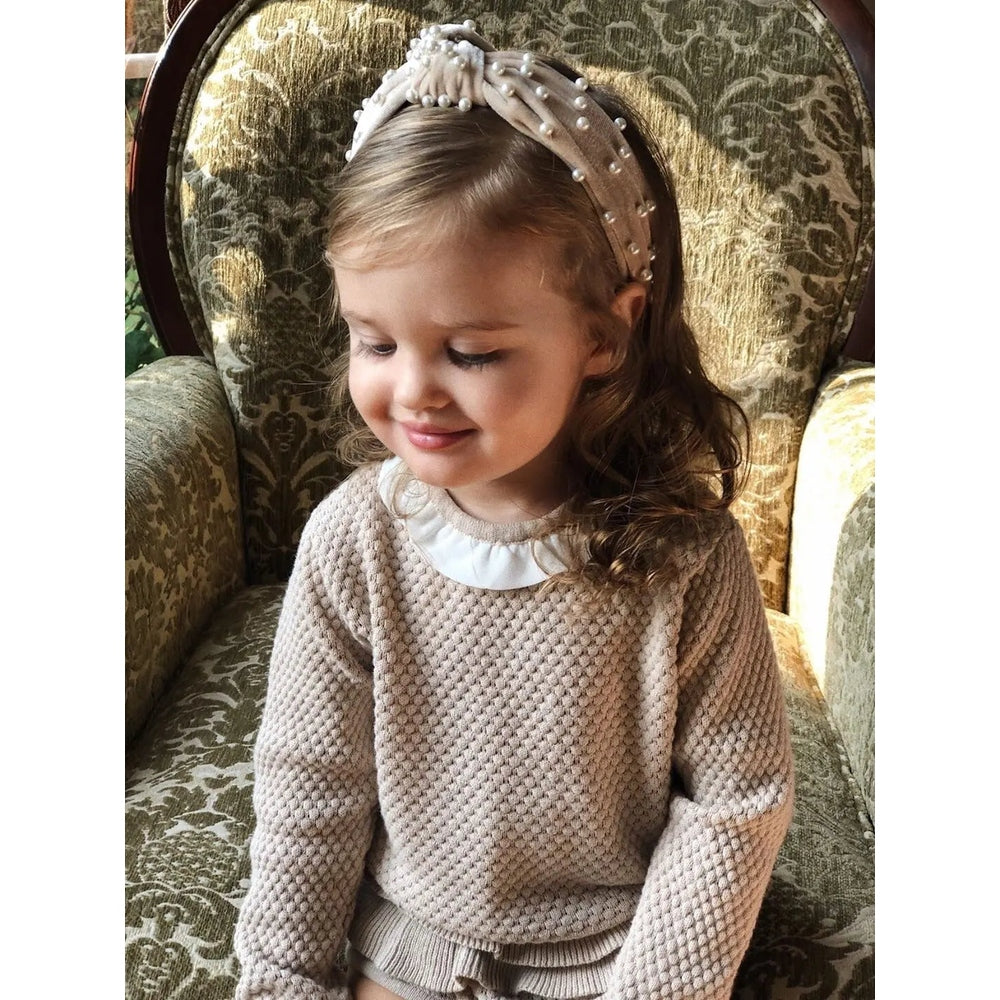 Petite Maison Kids Velvet Pearl Headbands on a smiling toddler, beige velvet band with pearl accents.