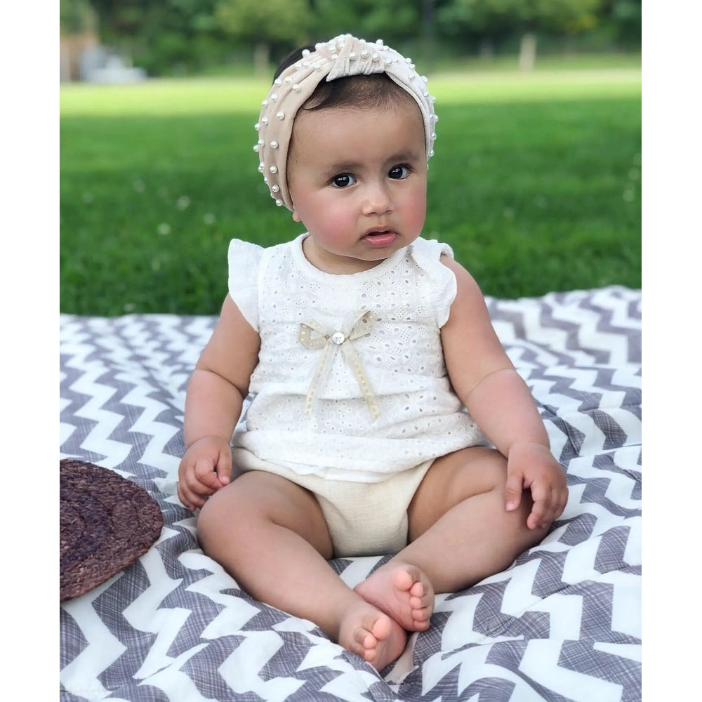 Petite Maison Kids Velvet Pearl Headband on a baby in cream dress; pearl-embellished velvet band shown as she sits on a chevron blanket outdoors.