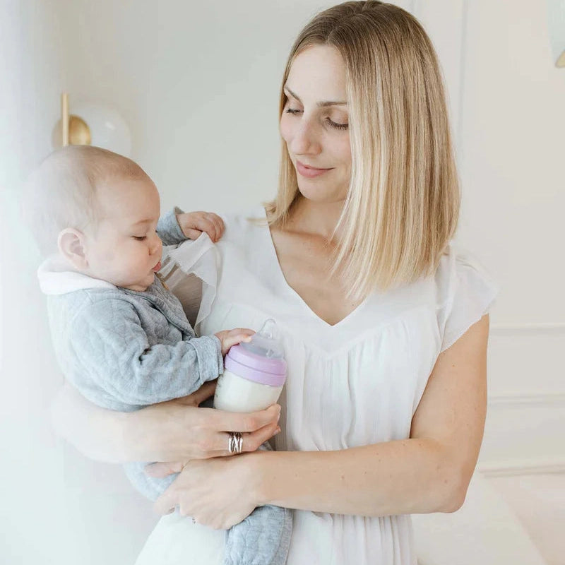 Quark Buubibottle Hybrid Feeding Bundle, lavender-cap bottle, mom feeds baby while cradling.
