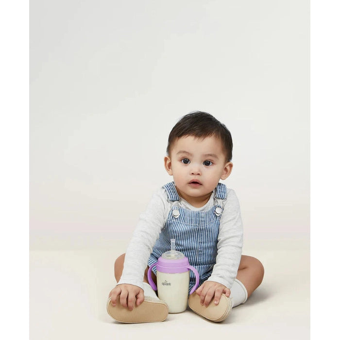 Quark Buubibottle Sip Toddler Sippy Cup With Straw sits beside a seated baby, lavender lid and purple handles visible.