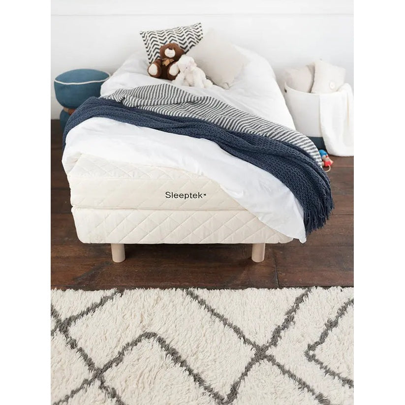 Sleeptek Organic Kids Rubber Mattress on a small bed with white quilt cover, navy blanket, and plush toys.