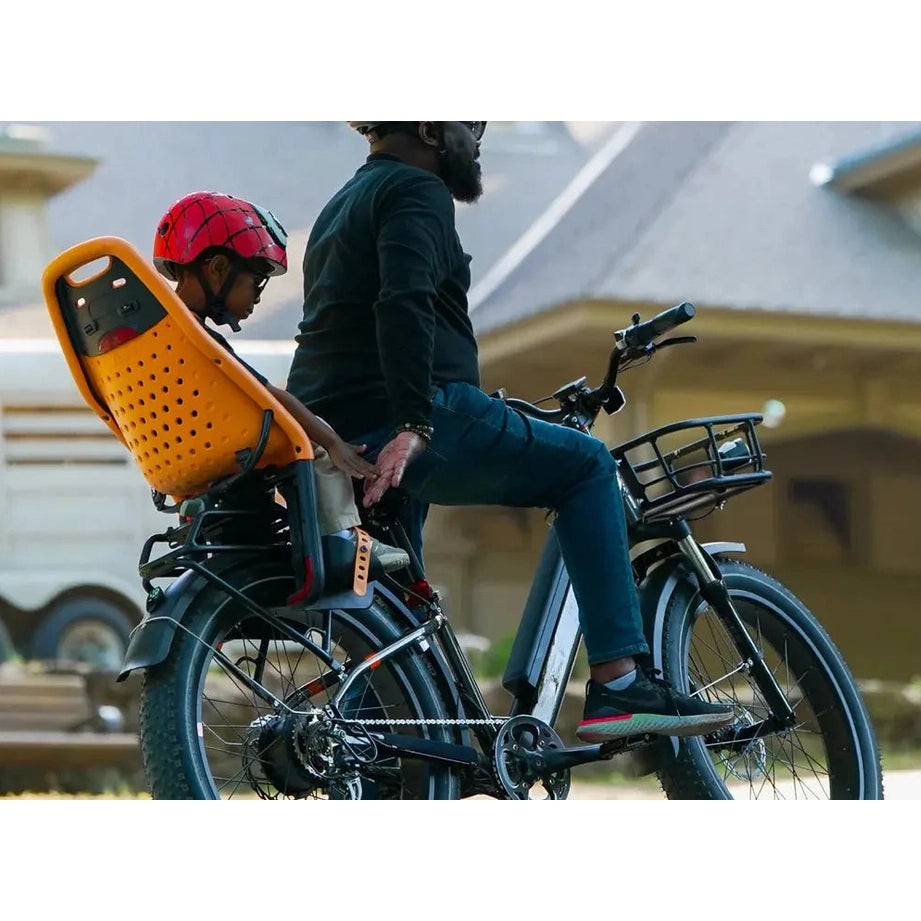 Thule Yepp Maxi rack-mounted child bike seat in orange, child wearing a red helmet seated on a bike.