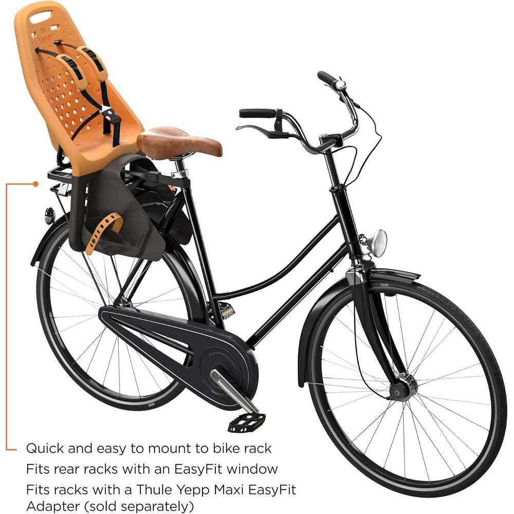 Thule Yepp Maxi rack-mounted child bike seat in orange, securely mounted on a black bicycle rear rack, harness visible.