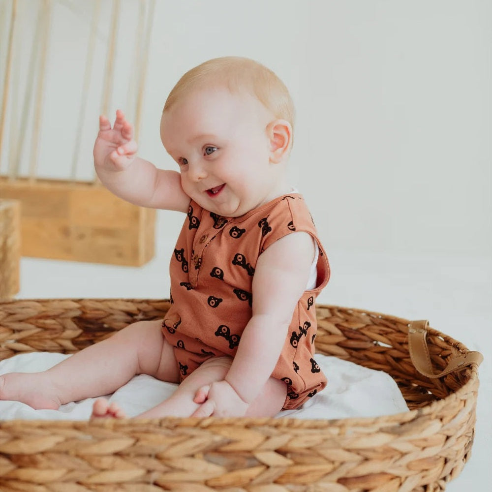 Turtledove London Two Bears Bubble Romper Sunset: cheerful baby in peach bear-print romper waves hello in a woven basket