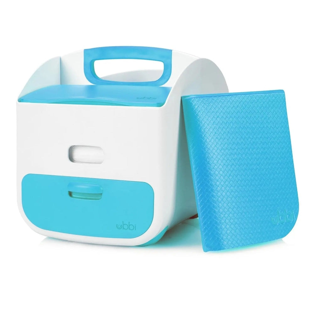 Ubbi Diaper Caddy in white with blue accents, shown with a matching blue changing mat propped beside it.