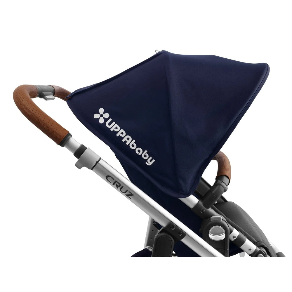 Uppababy Cruz Leather Handle Bar Cover in brown leather fitted to navy stroller, showing textured perforated grip.