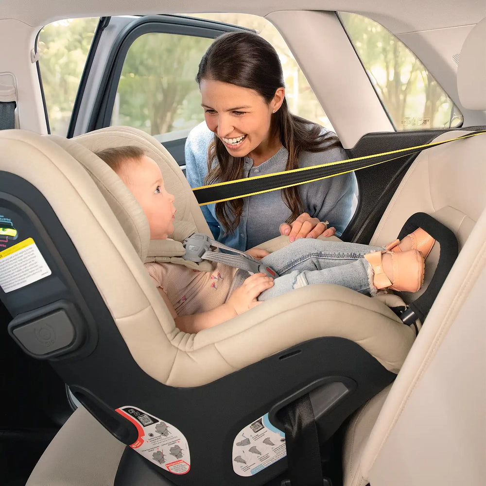 Uppababy Rove convertible car seat in beige; child buckled in and caregiver nearby.