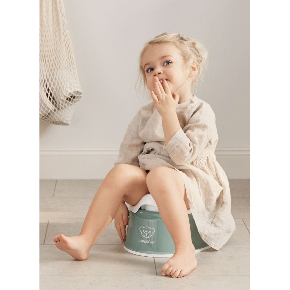 BabyBjörn Smart Potty in soft mint green with a girl sitting on it, practicing potty training.