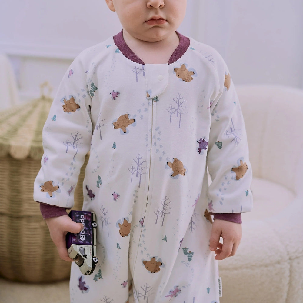 Nest Designs Organic Cotton Long Sleeve Footed Sleep Bag 1.0 Tog Snow Angels; cozy baby in white bear/snow print sleep sack, holding a toy car.
