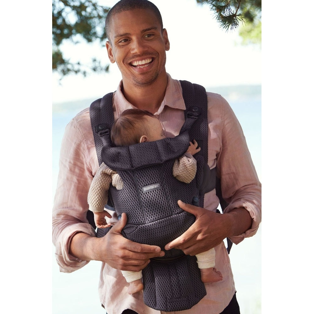 Father outdoors wearing the BABYBJÖRN Baby Carrier Free in dark gray, securely carrying a baby facing inward.