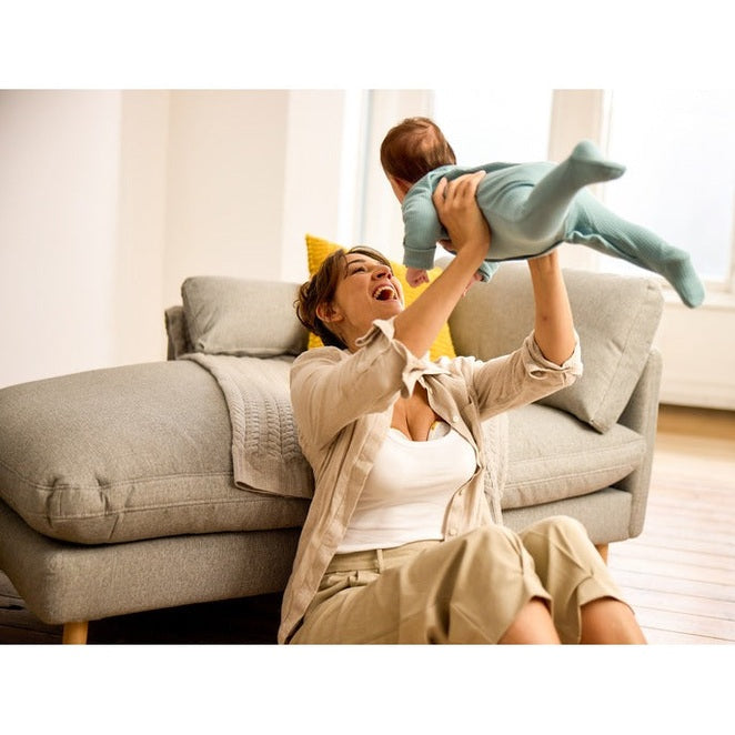 MEDELA Melody InBra Double Electric Breast Pump in a cozy living room; mom smiles, lifting baby for hands-free bonding.