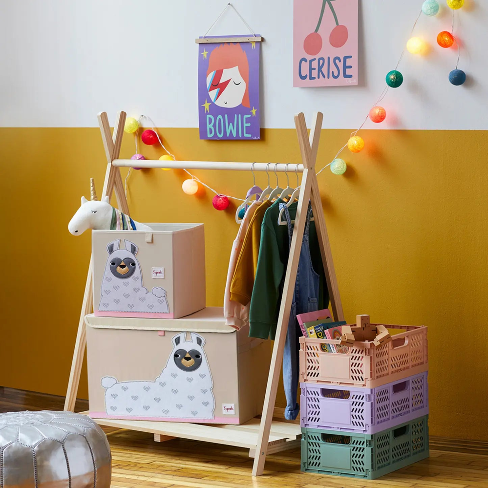 3 Sprouts Toy Chest with llama motif, plus matching pale pink boxes on a wooden rack in a cozy playroom.