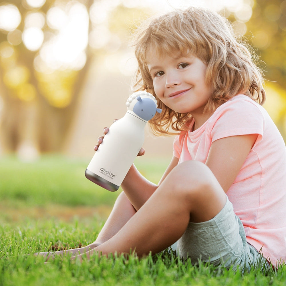 Asobu Bestie Animal Double Wall Stainless Steel Bottle 16oz Sheep held by a smiling girl in a sunlit park.