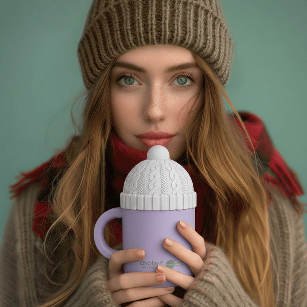 Woman wearing a knit hat and scarf, holding a purple mug with a white lid.