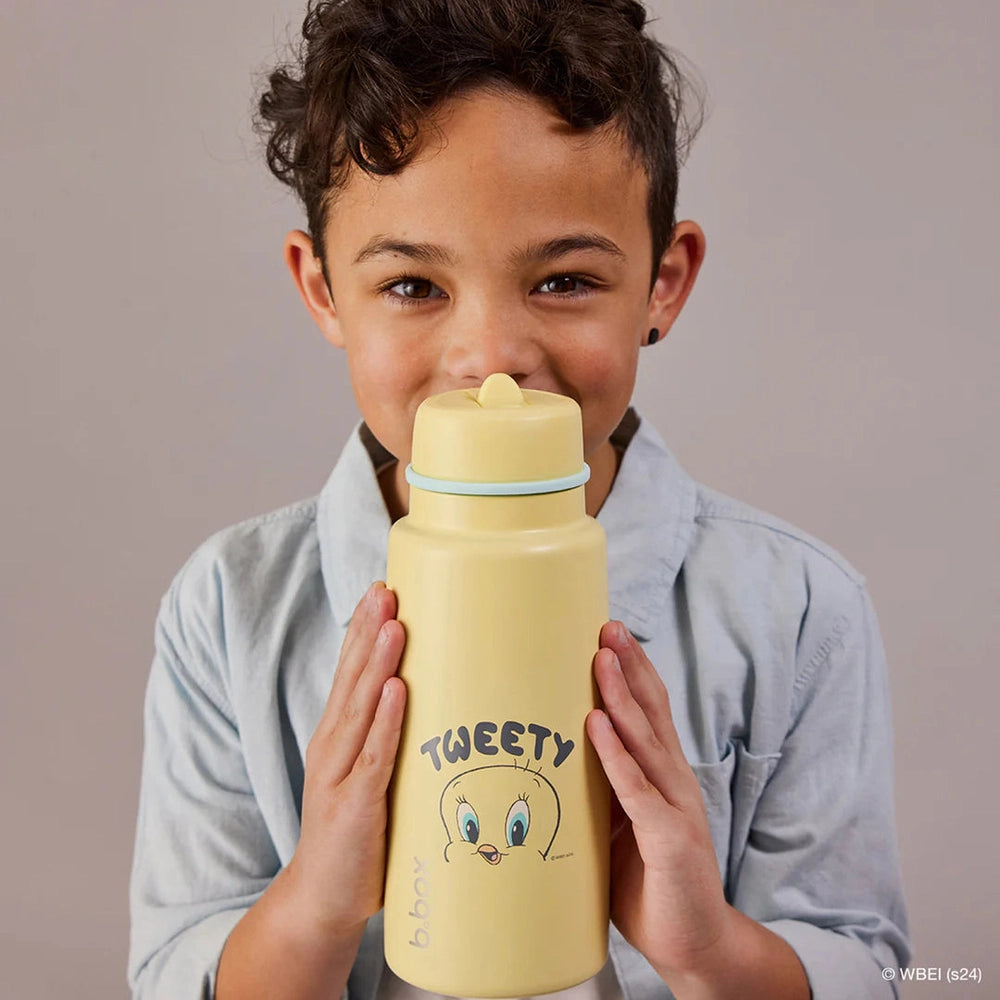 B.box Insulated Flip Top 1L yellow water bottle with Tweety design, held by a smiling child near the mouth.