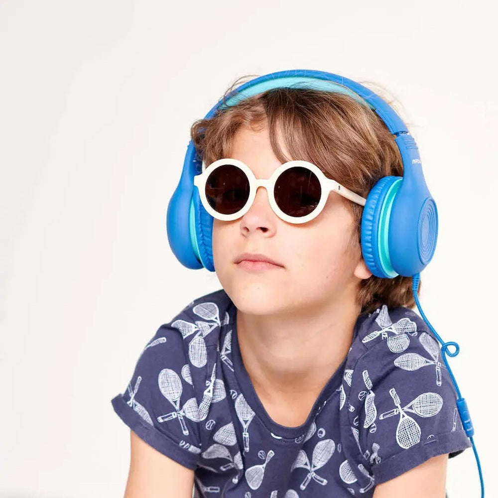 Babiators Euro Round Sweet Cream sunglasses worn by a child, white round frames with dark lenses, paired with blue headphones