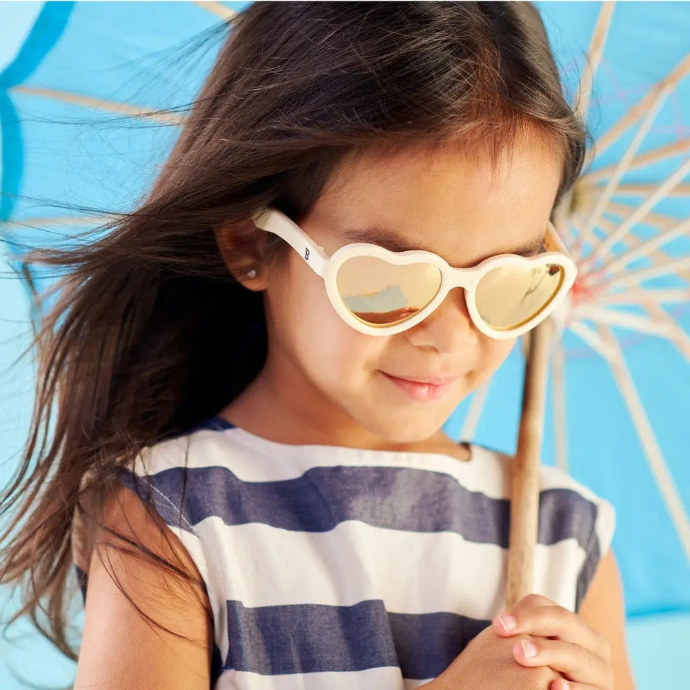 Babiators Polarized Mirrored Sunglasses Heart Shape Sweet Cream worn by a girl under a blue umbrella, mirrored lenses reflect the scene.