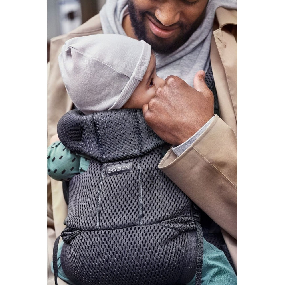 BabyBjörn Baby Carrier Free in dark gray mesh; caregiver holds baby close against chest.