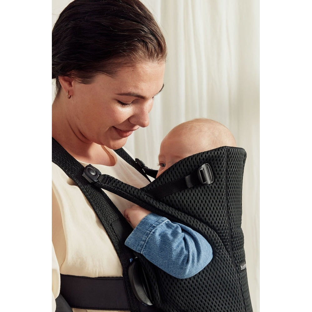 BabyBjörn Baby Carrier Free in black mesh, worn by a mother carrying her infant close to her chest with padded straps.