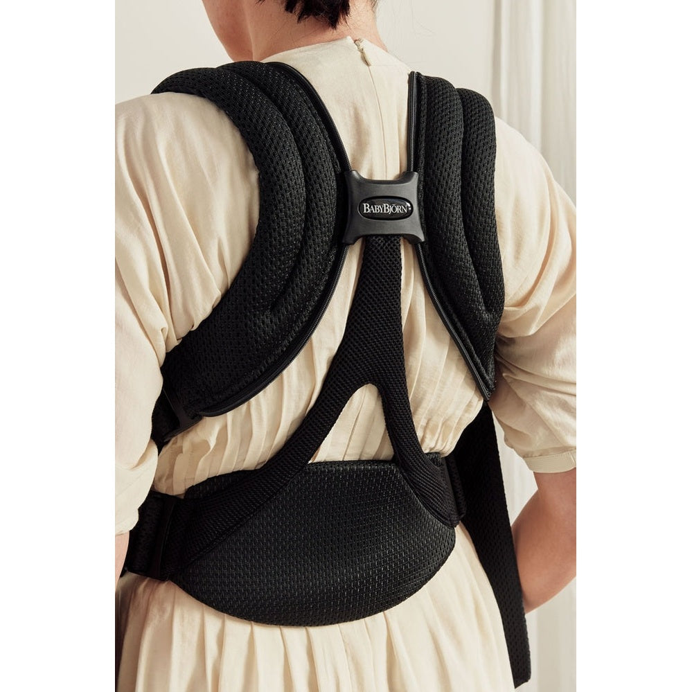 BabyBjörn Baby Carrier Free worn on a beige dress; ergonomic padded straps and waist belt secured around the back.